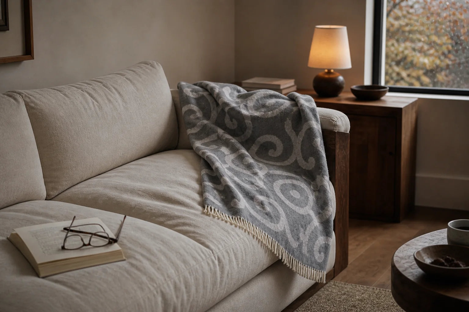 A grey patterned Sofia Toscano throw beside an open book in an autumn living room