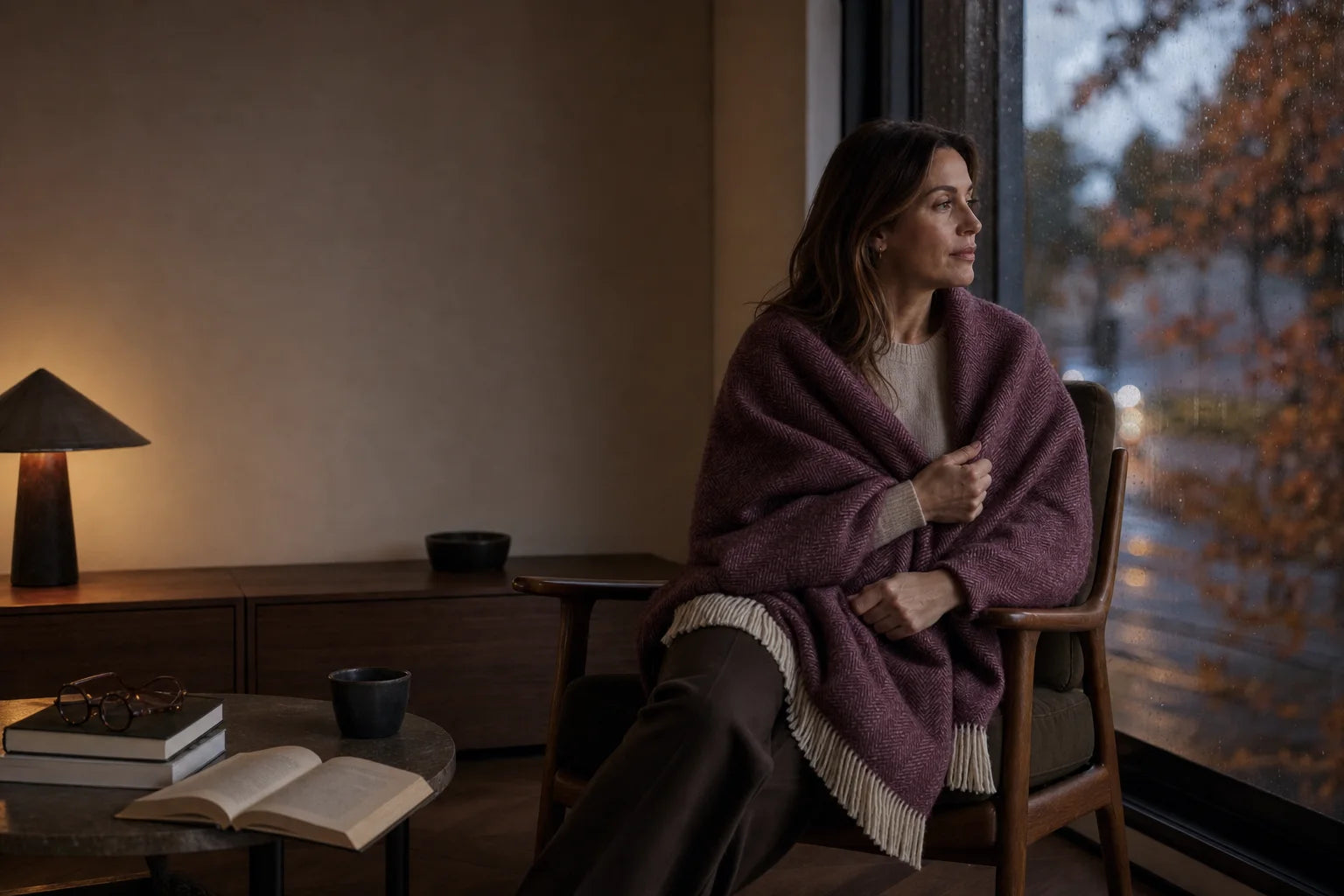 Woman wrapped in a burgundy herringbone throw beside a living-room window